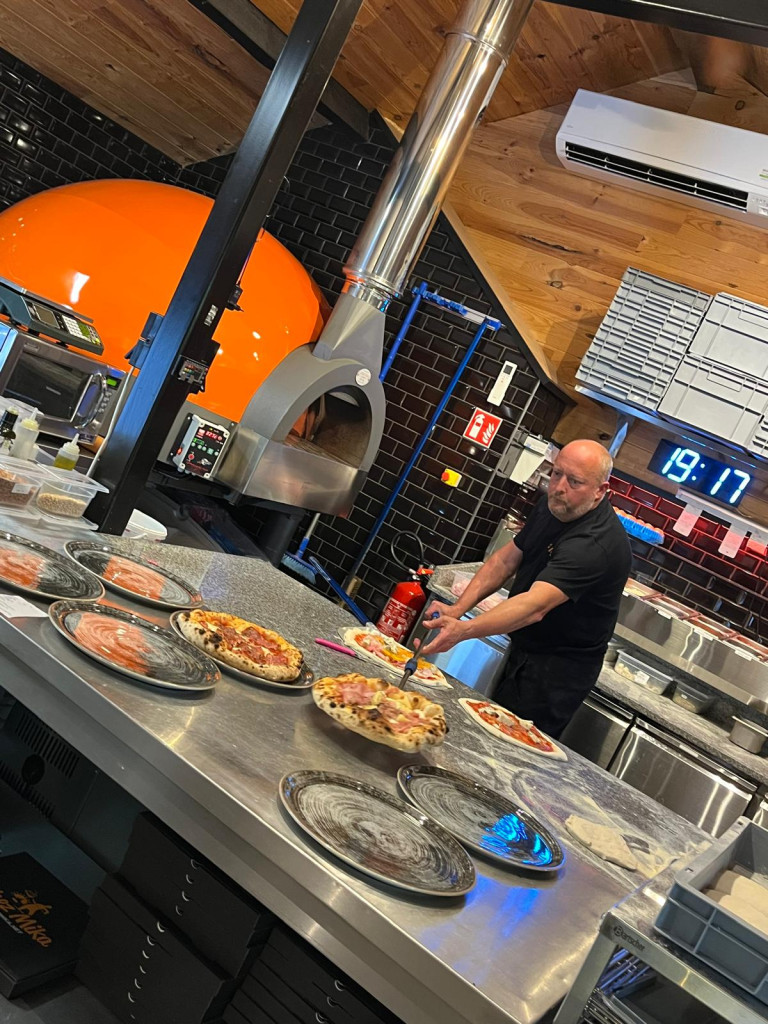 Mika occupé à sortir des pizzas du four, les déposant de belles assiettes